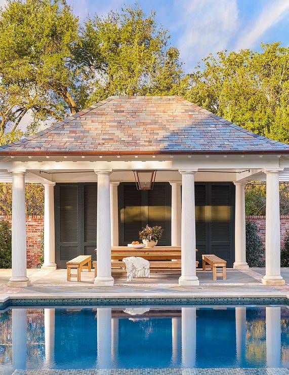 Gorgeous white pool house boasts Greek columns and is contrasted with black shutters doors.