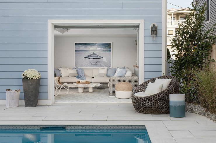 A small blue pool house is fitted with glass garage style doors.