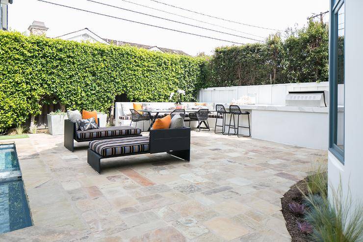 Black wicker outdoor chaise lounges on an outdoor patio completed with cobblestone pavers and backyard privacy hedges.