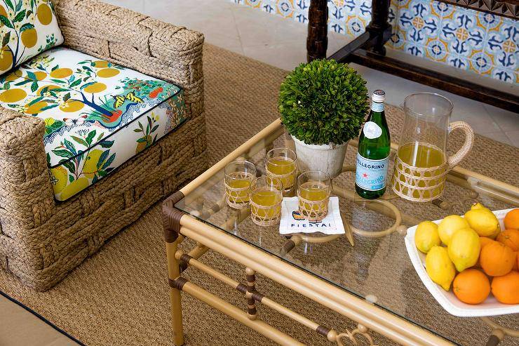 Placed on a seagrass rug, a woven chair with charming lemon print cushions is placed at a bamboo coffee table with a glass top.