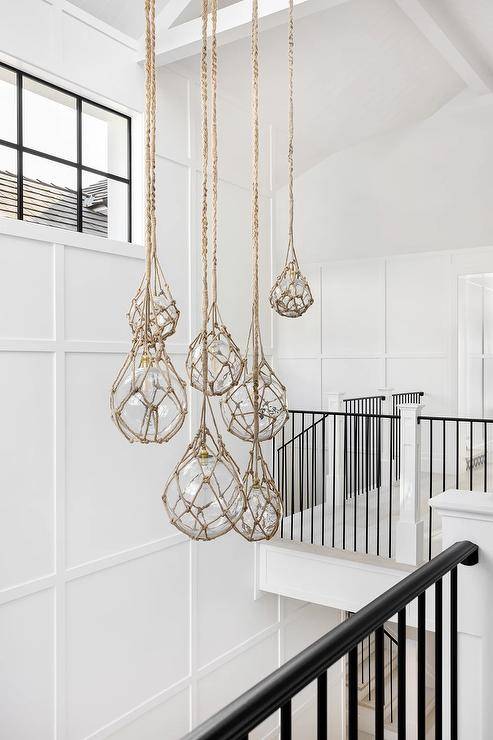 Staggered rope and seeded glass lanterns light a board and batten staircase wall.