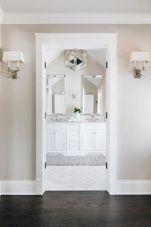 Beautiful master bathroom boasting white and taupe color tones accented with elegant finishings and stylish fixtures. A mercury glass chandelier brings a unique and luxurious appeal with a geometric touch in a spa-like bathroom design.