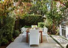 Outdoor patio design featuring tall green privacy hedges and shrubs creating an enclosure around a wood patio table and white modern chairs.