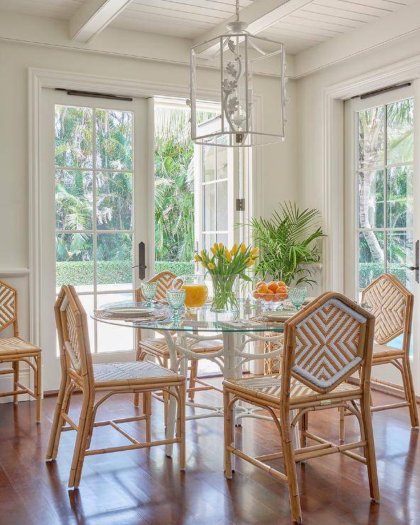 Cottage dining room furnished with rattan hexagon chairs at a white bamboo table illuminated with a white lantern hanging from a white wood plank ceiling.