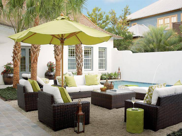 Relax poolside beneath a lime green umbrella accenting a lime green stool table and lime green pillows placed atop dark brown wicker chairs and facing dark brown wicker sofas finished with white seat cushion. The seating area is centered around a dark brown wicker coffee table placed on a gray shag rug.