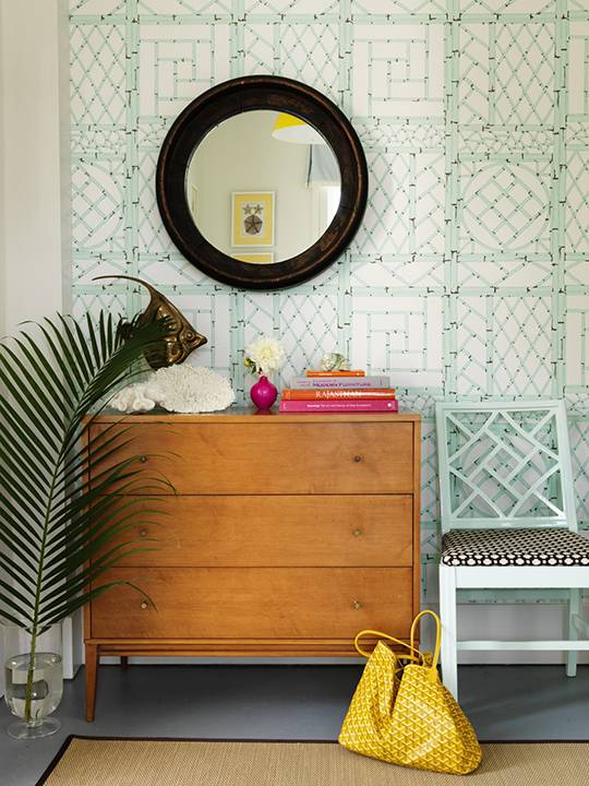 Tropical foyer design with mint green blue fretwork wallpaper, mint green blue lattice chair, round wood mirror, vintage chest and sisal rug.