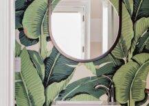 Jungle palm leaf wallpaper in a powder room transforms a look into a lush, tropical escape. Wall mount sink with a mod chrome faucet complements a chrome towel rack on the base of the sink under a round black mirror lit by a two-light linear globe sconce.