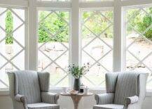 Gray stripe wingback chairs in sit in front kitchen bay windows finished with mullion trim.