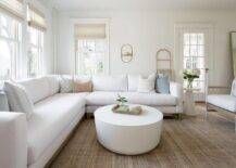 Living room features a white sectional accented with blue pillows and a round white coffee table on a tan rug.