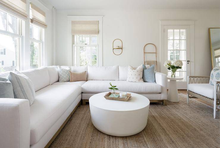 Living room features a white sectional accented with blue pillows and a round white coffee table on a tan rug