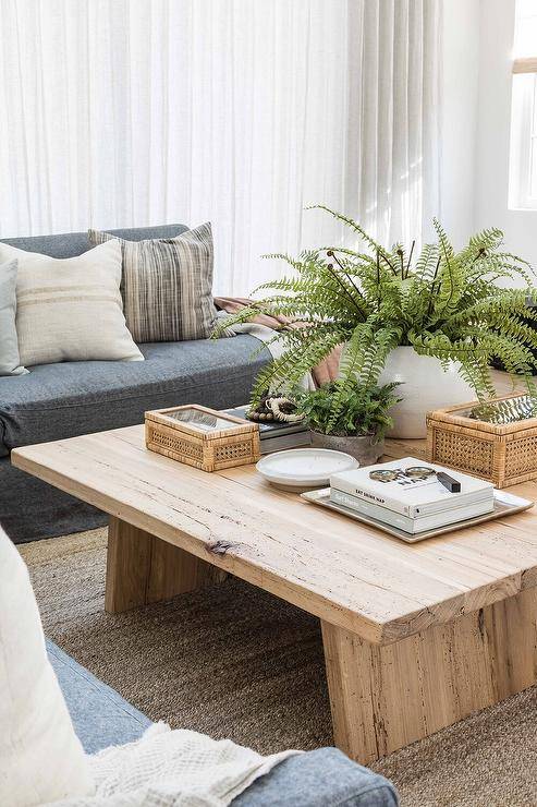 A potted fern sits on a salvaged wood coffee table placed on a light brown jute rug in front of a charcoal gray sectional topped with white and gray pillows.