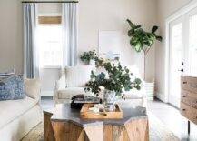 Wood and concrete starburst coffee table surrounded by a linen sofa, a stripe cream accent chair, and a fiddle leaf fig plant in the corner of the living room.