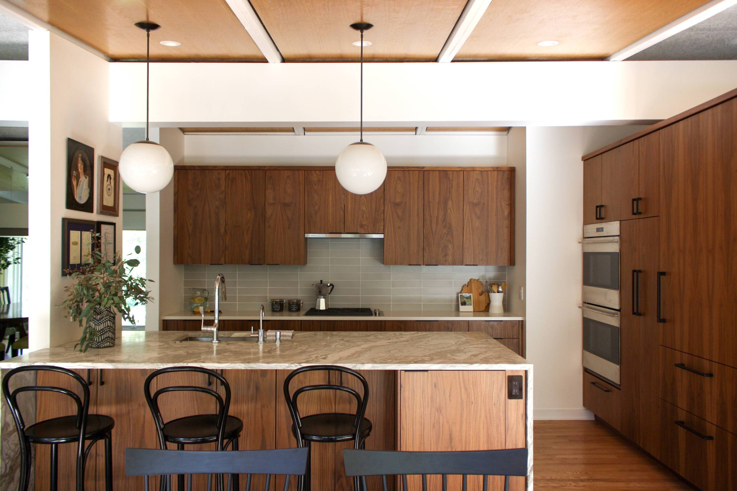 A clean mid-century kitchen with dark wood cabinets, black metal chairs, and an island with a sink.