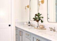 Bathroom features a double gray bath vanity with brass pulls, nickel mirrors flanked by glass and brass sconces, a marble countertop with nickel faucet, and a vintage rug on marble basketweave floor tiles.
