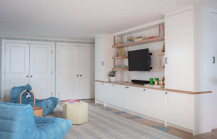 Basement playroom boasts a modern two-tone TV cabinet built-in under a wall mount TV framed by wood floating shelves mounted between white cabinets.