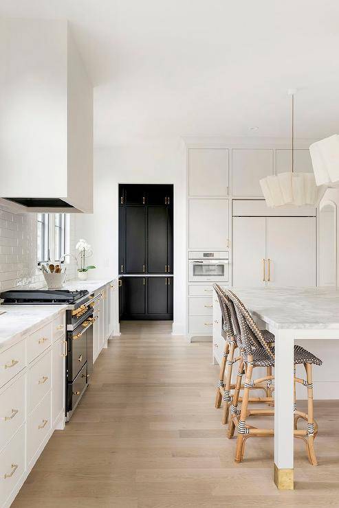 Ruffled linen pendants hang over a honed marble countertop accenting a white kitchen island matched with black and white French bistro stools.