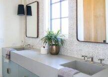 Bathroom features curved brass mirrors mounted on whitewashed vintage tiles over a sky blue double bath vanity that boasts brass pulls, topped with gray quartz.