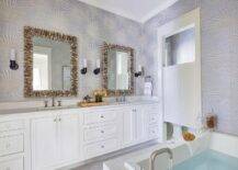 Elegant bathroom boasts seashell mirrors hung from a wall covered in silver and blue starburst wallpaper over a white dual washstand adorned with nickel knobs and finished with polished nickel faucets lit by oil rubbed bronze sconces.