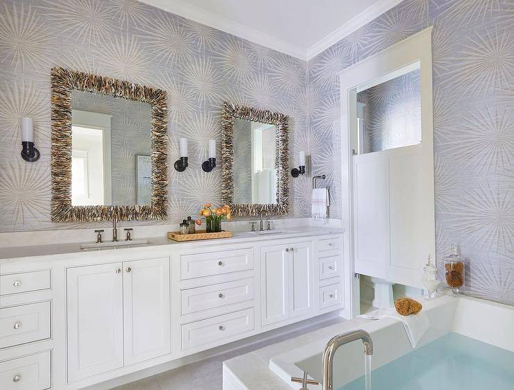 Elegant bathroom boasts seashell mirrors hung from a wall covered in silver and blue starburst wallpaper over a white dual washstand adorned with nickel knobs and finished with polished nickel faucets lit by oil rubbed bronze sconces.