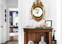 Entryway features an antique console table with black marble countertop boasting Chinese ginger jars, underneath a gold eagle mirror, vertical plank foyer wall and a boots umbrella holder.