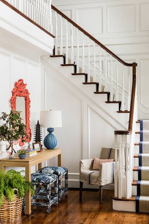 Eclectic entryway with full wall wainscoting framing an Asian style console table topped with a pagoda sculpture and a blue urchin lamp with a coral pink Baroque mirror above and a pair of stools upholstered in Chiang Mai Dragon - China Blue fabric below across from a French grain sack slipcovered chair.