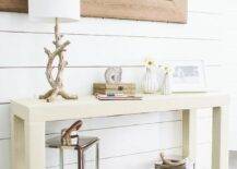 Beach entryway with a pair of Country Chic Fisherman's Lanterns tucked below a cream parsons console table which is topped with a driftwood table lamp, framed photo and urchin bud vase highlighted by a shiplap clad backdrop wall adorned with a rustic wood framed mirror.