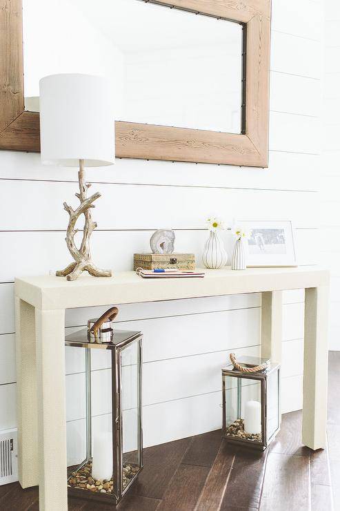 Beach entryway with a pair of Country Chic Fisherman's Lanterns tucked below a cream parsons console table which is topped with a driftwood table lamp, framed photo and urchin bud vase highlighted by a shiplap clad backdrop wall adorned with a rustic wood framed mirror.