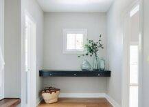 Entryway designed with a black floating console table displaying recycled glass vases boasting gray painted walls and wood floors.