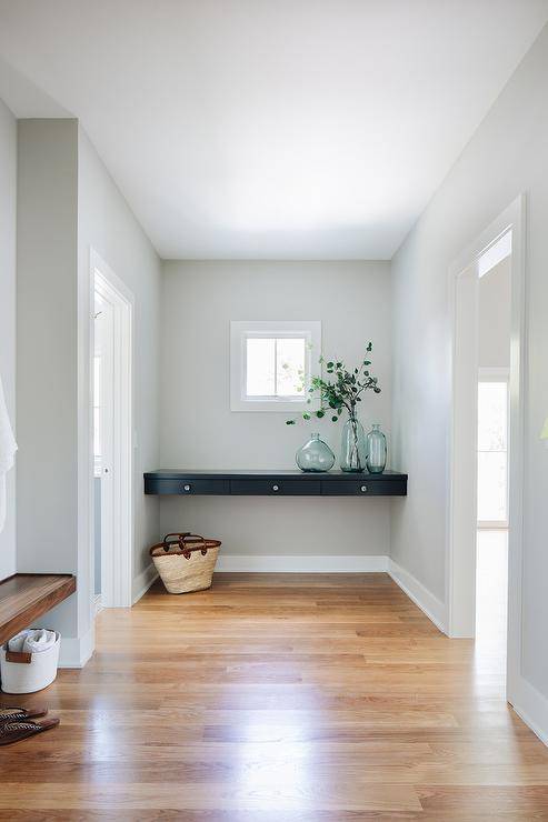 Entryway designed with a black floating console table displaying recycled glass vases boasting gray painted walls and wood floors.