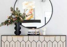 Entryway features a white and gold credenza with black vase under a round black mirror.