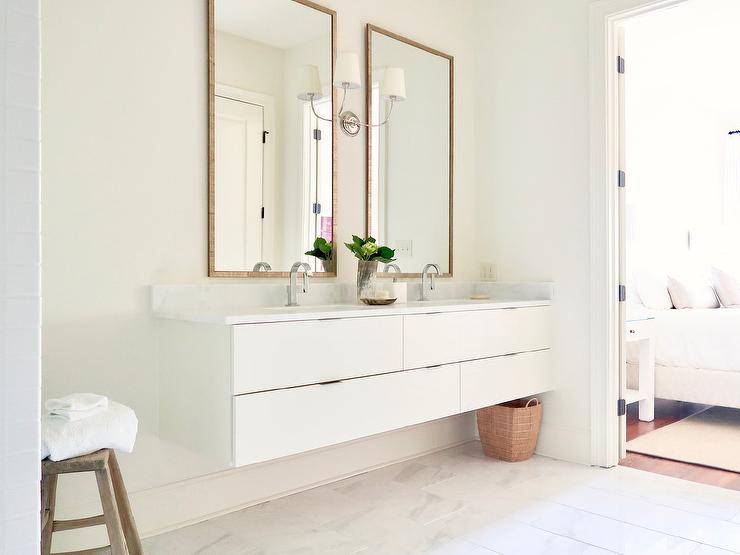 Woven mirrors are mounted above a white floating dual washstand finished with modern chrome faucets.