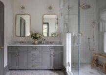 A gray wooden dual bath vanity dons polished nickel hardware and a gray marble countertop holding polished nickel cross handle faucets under curved nickel mirrors lit by nickel and glass sconces.