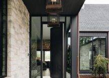 Industrial cage lanterns lead to a black chevron door flanked by sidelights and located under a transom window.
