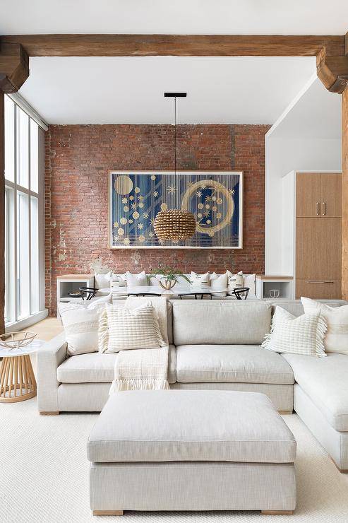 White fringe pillows on a light gray sectional in a condo loft room with red brick exposed walls.