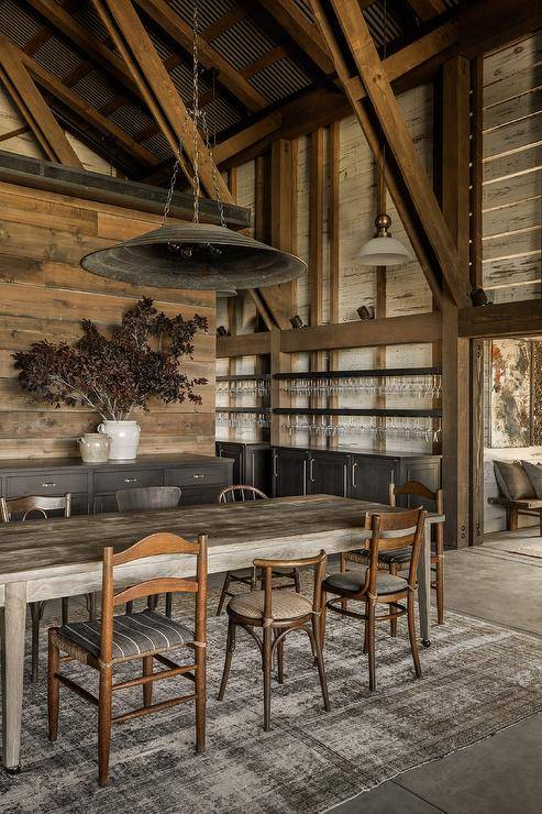 Cottage dining room features mismatched vintage chairs at a rustic oak farmhouse dining table lit by an industrial pendant hung from a truss ceiling and a black overdyed rug.