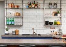 Kitchen features blue bar cabinets with concrete countertops and stainless steel industrial shelves on white offset tiles.