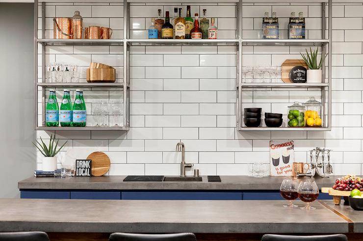 Kitchen features blue bar cabinets with concrete countertops and stainless steel industrial shelves on white offset tiles.
