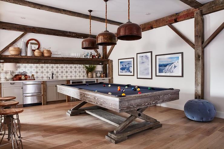 Accented with rustic wood beams, this charming media room boasts a gray oak pool table positioned beneath three copper industrial light pendants.