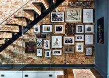 Eclectic foyer boasting a floating-style staircase and an exposed brick wall finished with gallery wall art in various placements and frames.