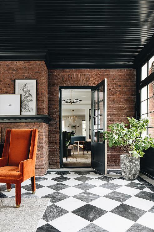 Stylish black sunroom features a glossy black plank ceiling lined with black crown moldings accenting a red brick wall and black and white harlequin floor tiles.