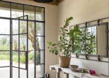 Cottage style foyer features a reclaimed wood console table under a long rectangular iron mirror, a steel and glass front door and a plank ceiling with wooden beams.