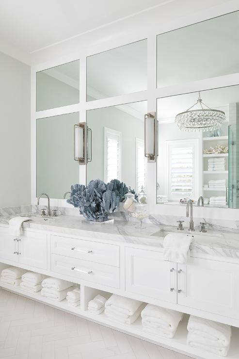 Inset vanity mirrors lit by cylinder sconces are stacked over a white dual washstand fitted with a towel shelf, nickel and glass pulls, and a gray marble countertop completed with polished nickel gooseneck faucets.