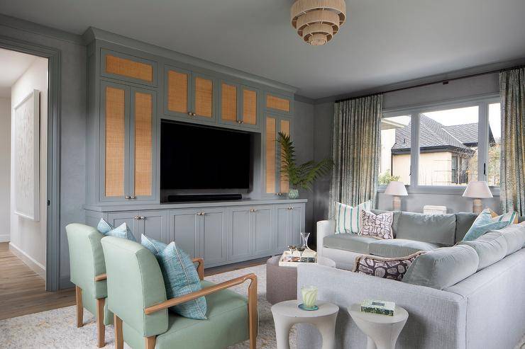 Family room features a gray velvet sectional accented with turquoise blue striped pillows, a blue built in TV unit with cane cabinet doors and green accent chairs with blue pillows.