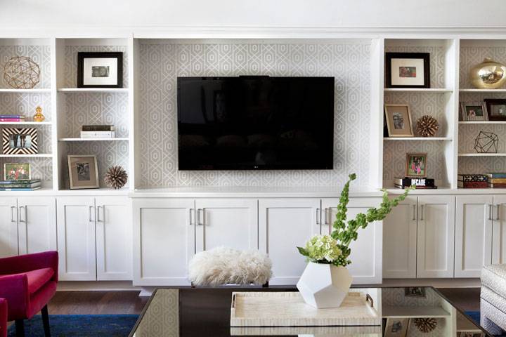 Transitional living room features a wall to wall white built in shelving unit lined with a flat screen TV and grey trellis wallpaper on the back of shelves.