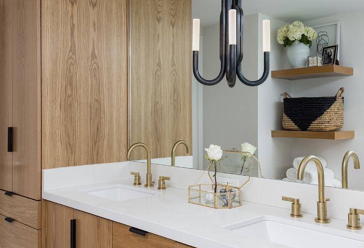 Bathroom features a Kelly Wearstler Rousseau double wall sconce on a vanity mirror over a wooden washstand with white countertop and dual brass faucets.