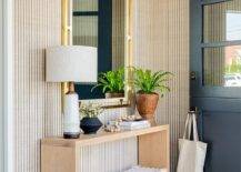 Entryway features white rope benches under a tan oak table, a brass and wood mirror on tan and black vertical stripe wallpaper, a blue and gray rug and a black Dutch door.