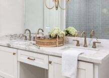 Brass hardware complements a white shaker washstand donning a marble countertop and dark nickel faucets fixed beneath a frameless vanity mirror finished with a Reed Double Sconce.