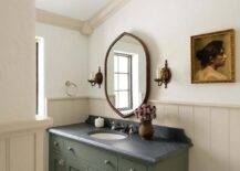 Bathroom features a forest green wooden washstand with honed black marble counter under a vintage mirror flanked by vintage sconces on cream plank trim.