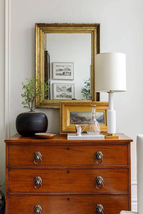 A baroque mirror hangs over a styled vintage chest of drawers.
