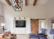 Family room with a barn door on rails encloses a space with a built-in entertainment center, a set of barn sconces and a set of blue pillow top spindle chairs with matching ottomans.